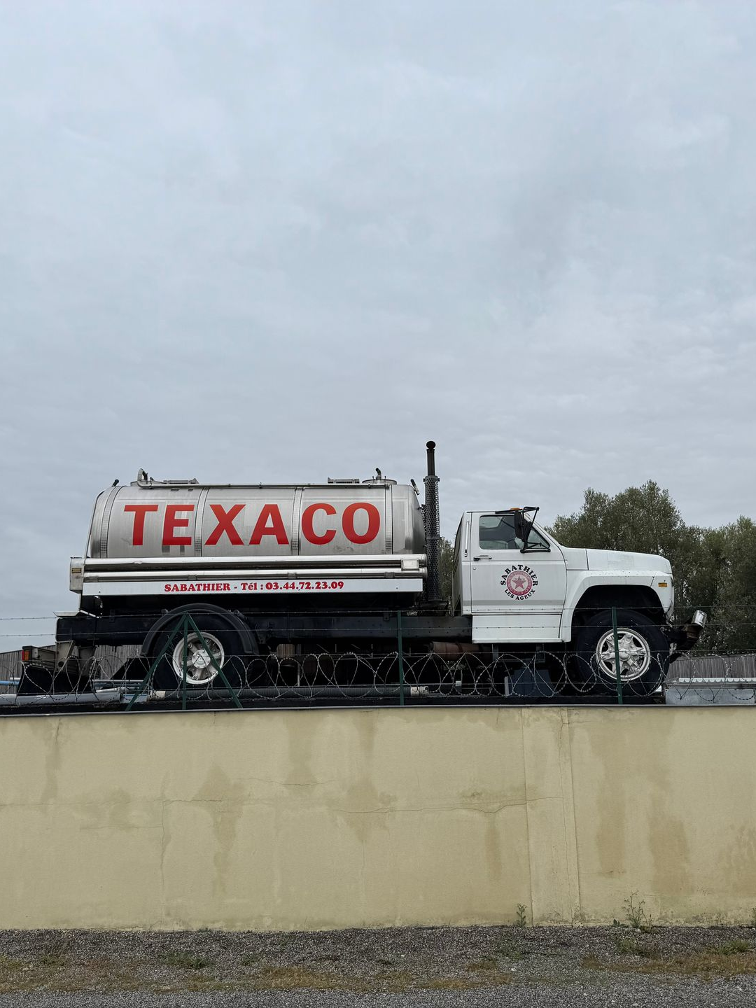 Camion-citerne Texaco blanc sur une plate-forme en béton contre un ciel nuageux.