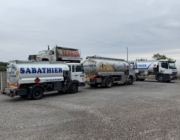 Quatre camions-citernes garés sur du gravier ; ciel nuageux au-dessus. Sabathier est visible sur l'un d'eux.