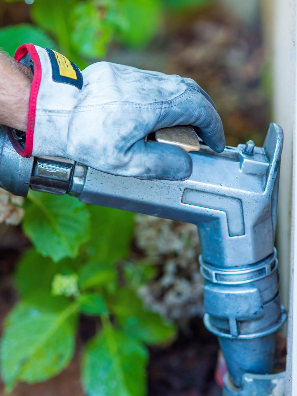 Main dans un gant de travail actionnant une buse de carburant argentée.