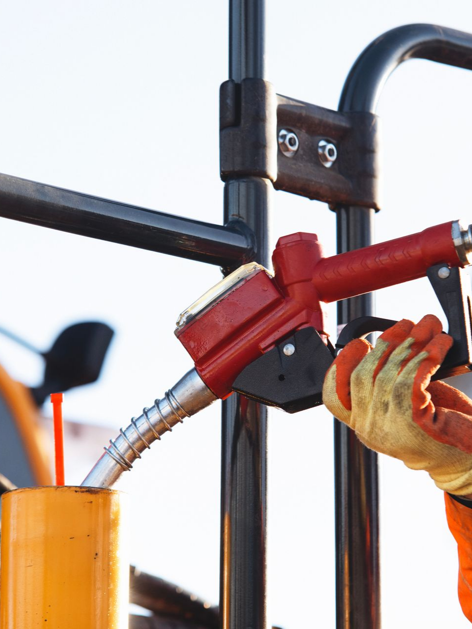 Une personne remplit un récipient jaune avec du carburant à l'aide d'une buse rouge ; la main gantée du travailleur est visible.