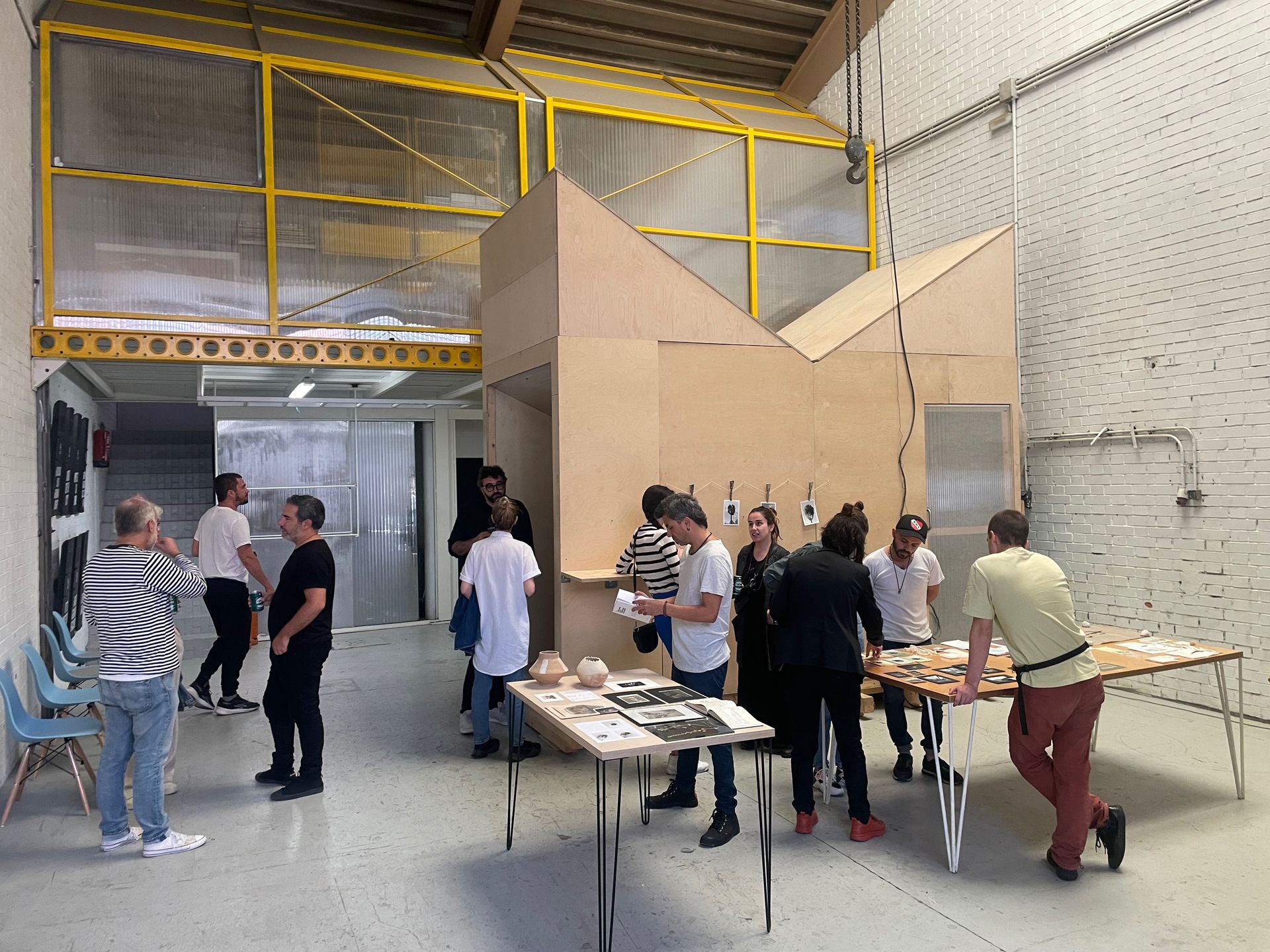 Personas en una gran sala con estructura de madera y mesas exhibiendo artículos.