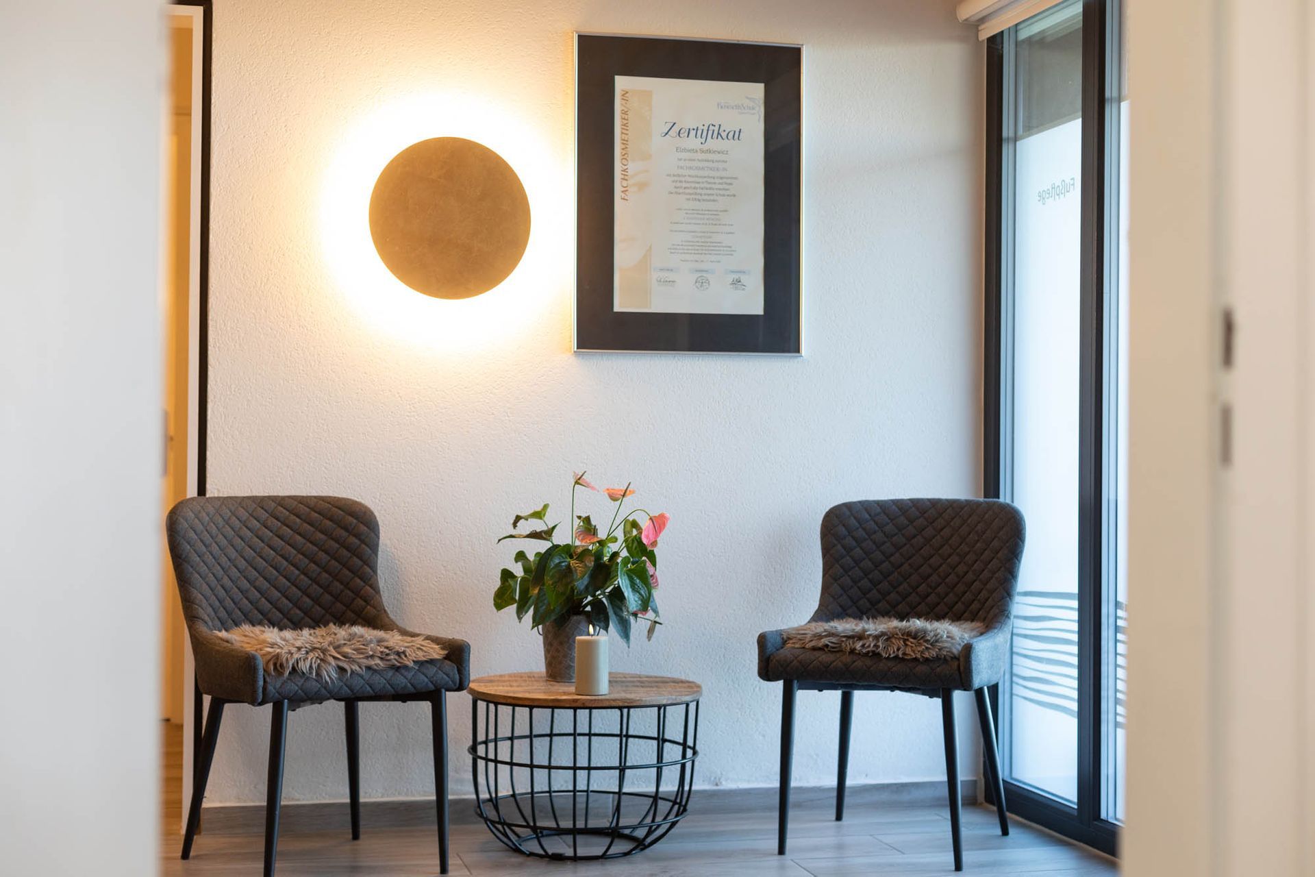 Ein Wartezimmer mit zwei Stühlen und einem Tisch mit einer Vase mit Blumen darauf.