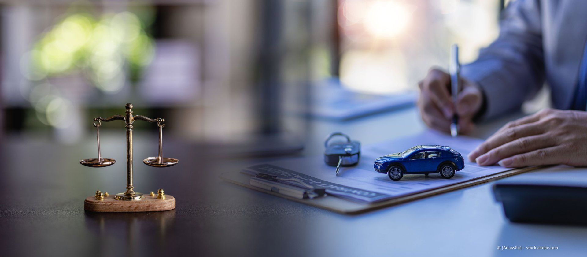 Eine Person füllt neben einem Spielzeugauto und einer Justitia-Waage Formulare aus.