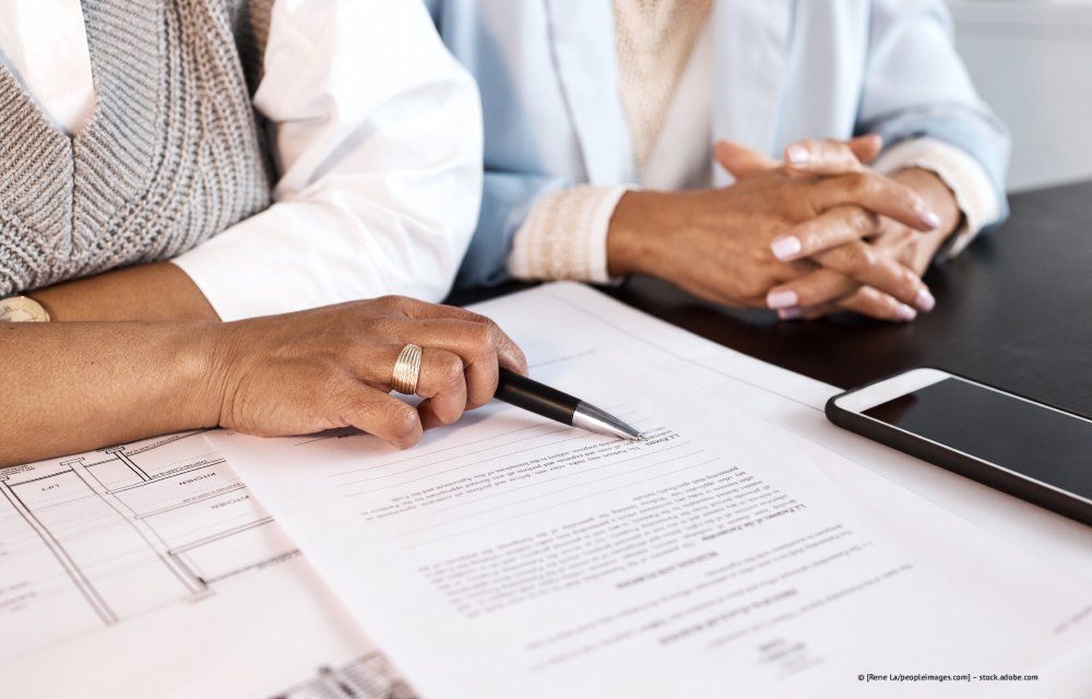 Die Hände zweier Personen, die mit Stift und Handy auf einem Tisch ein Dokument durchgehen.