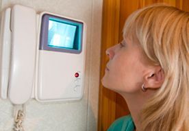 Una persona con cabello rubio mirando una pantalla de videoportero montada en la pared.