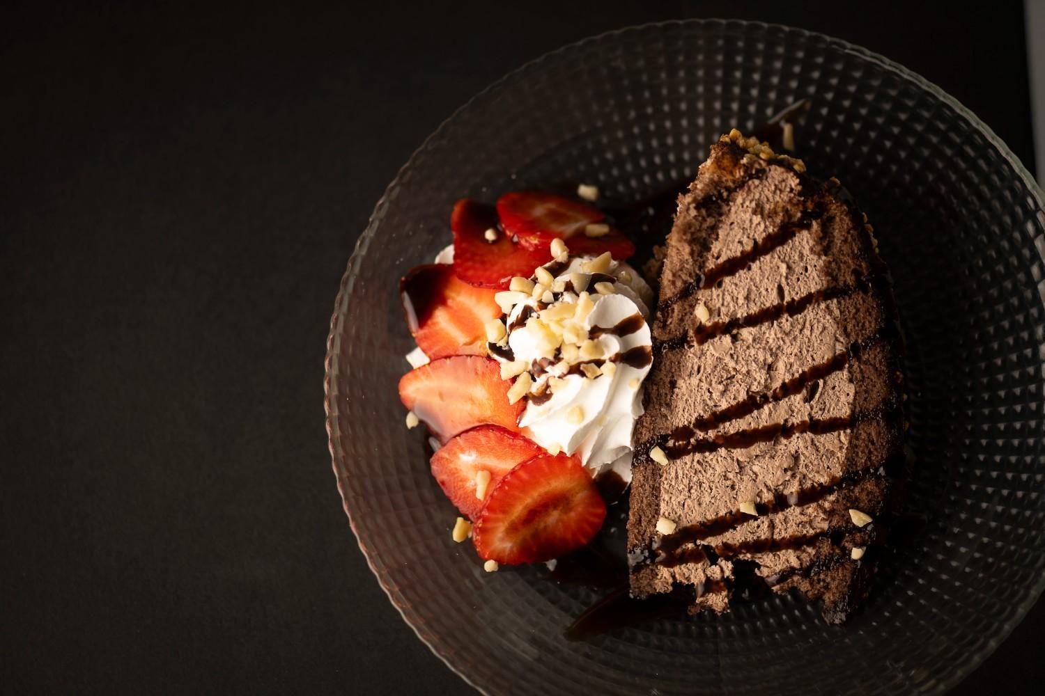 Postre de chocolate con fresas en rodajas, crema batida y nueces en un plato negro.