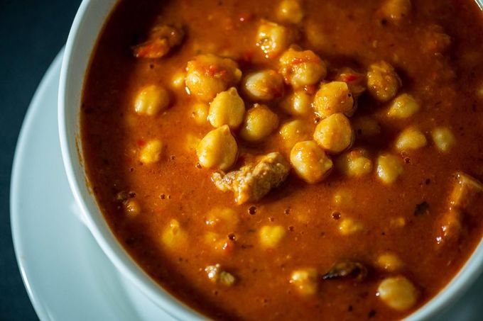 Bol de estofado de garbanzos en una rica salsa de color naranja rojizo con algunos trozos de carne visibles.