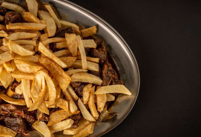 Un recipiente de metal lleno de papas fritas doradas sobre una superficie oscura.