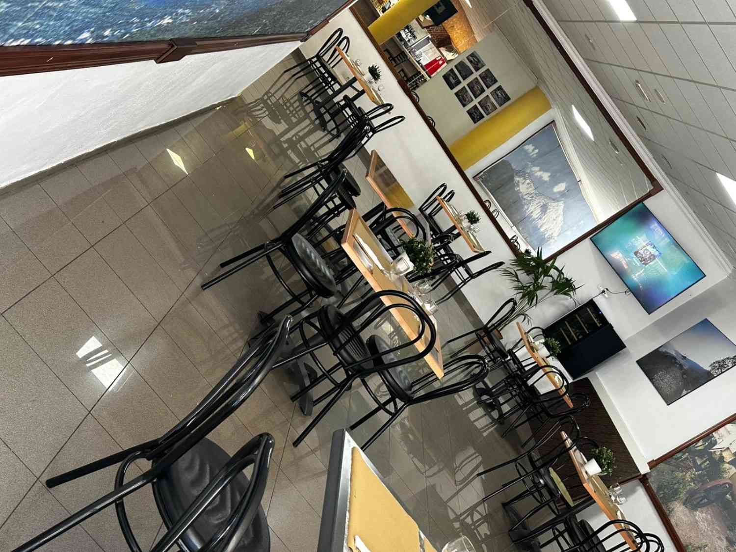 Cafetería vacía con sillas y mesas negras sobre un suelo de baldosas, vista desde un ángulo.