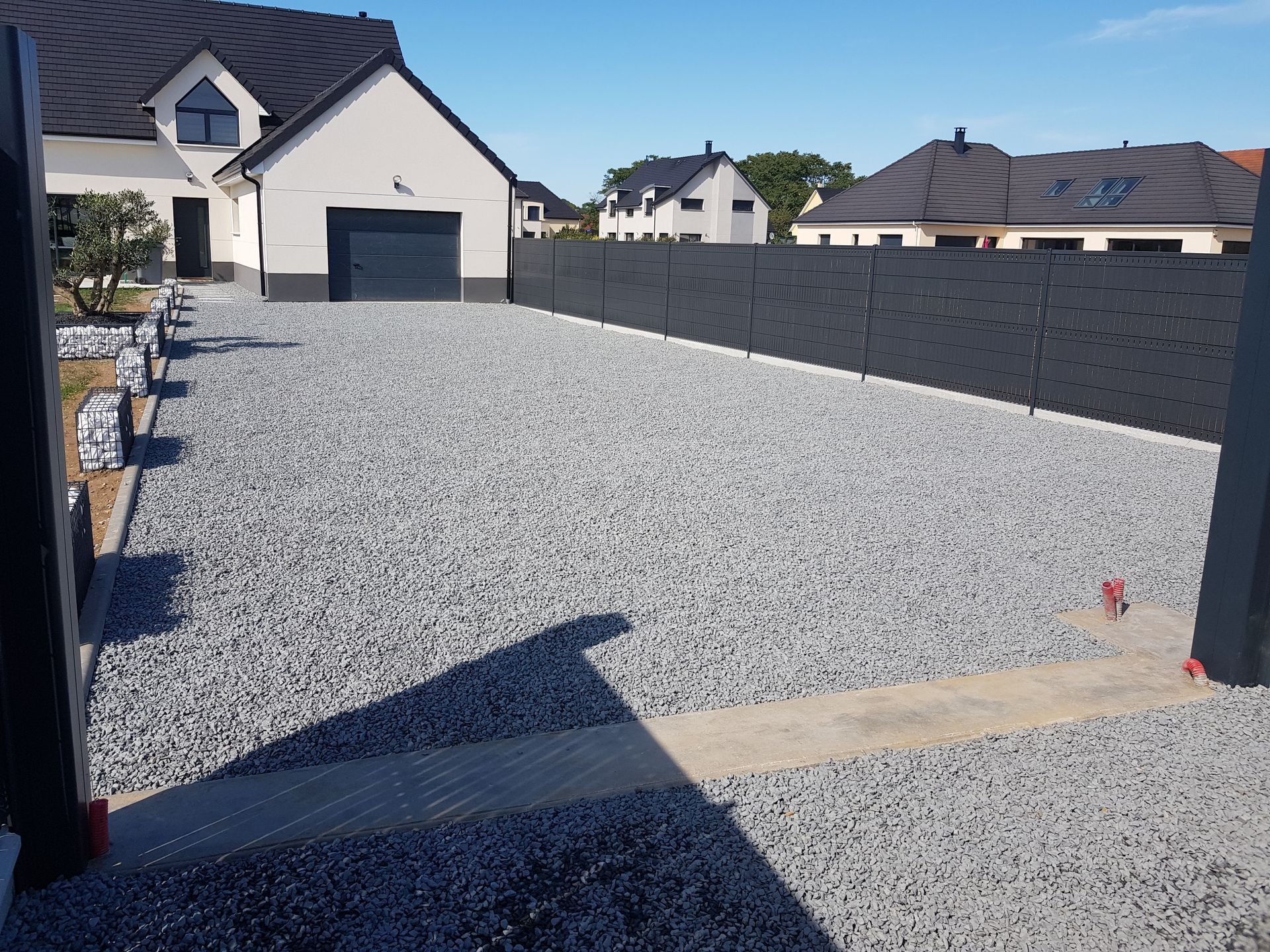 Aménagement extérieur - allée en gravier gris avec clôture occultante noire