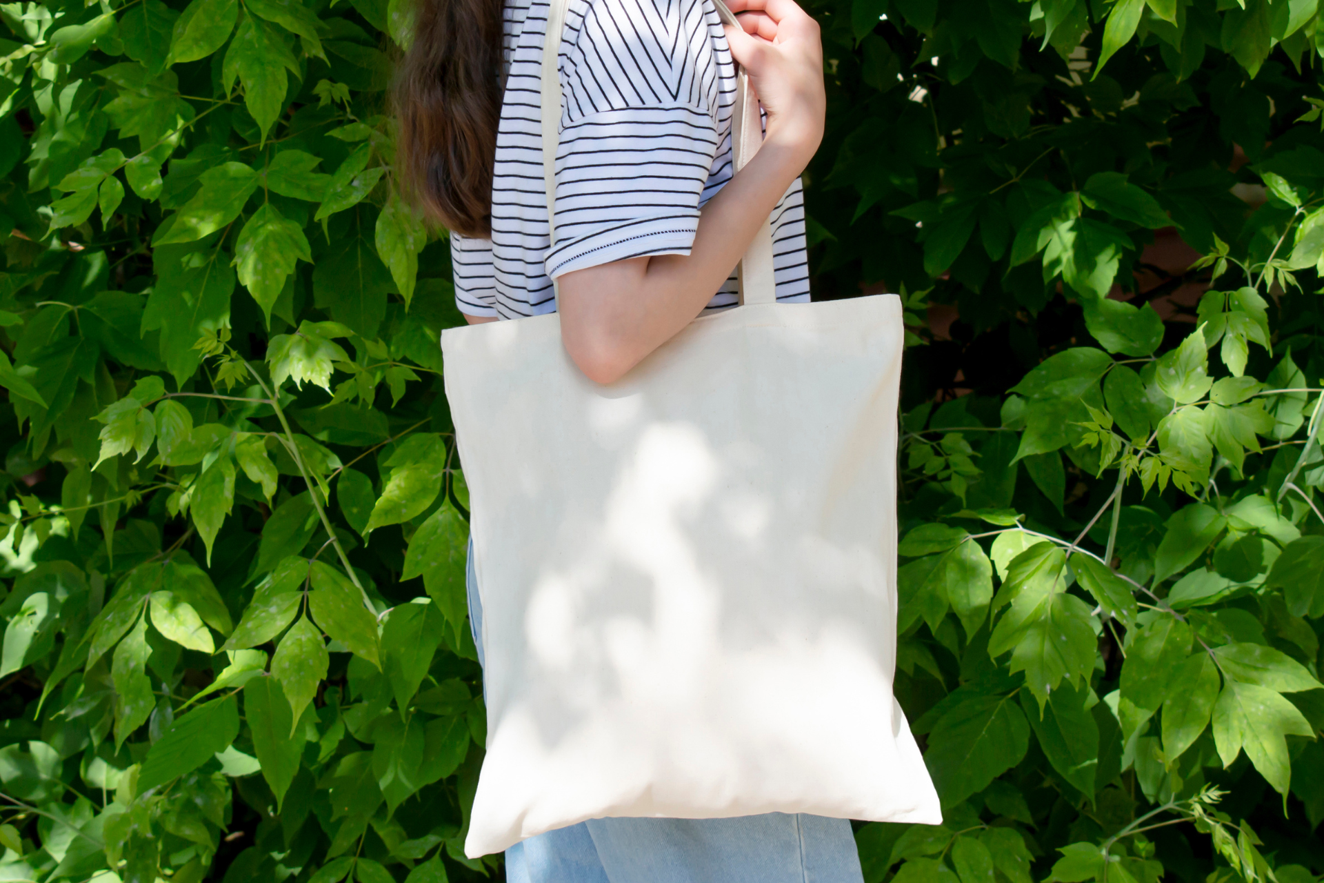 Una mujer sostiene una bolsa blanca frente a un árbol.
