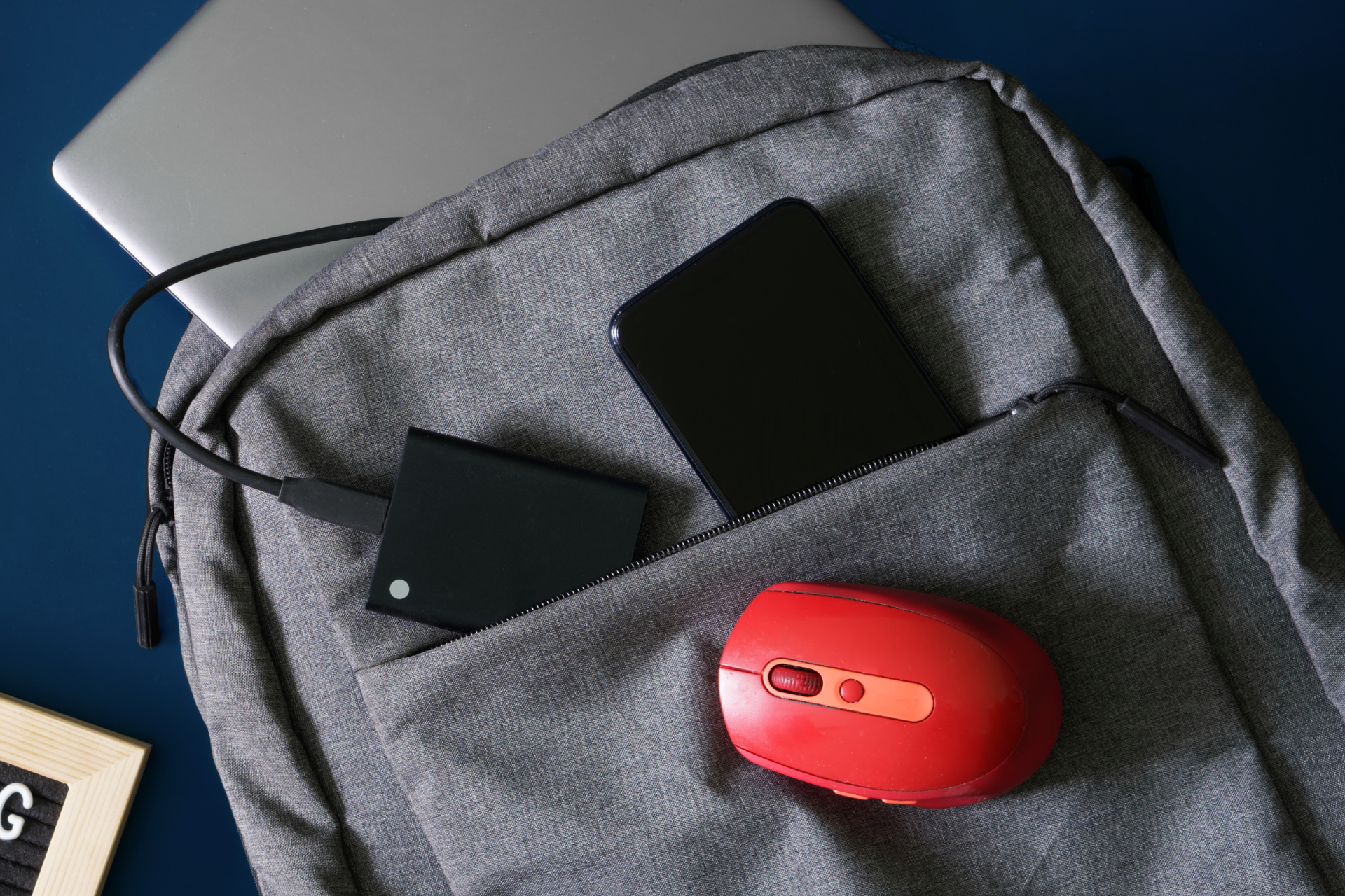 Un ratón rojo está en el bolsillo trasero de una mochila.