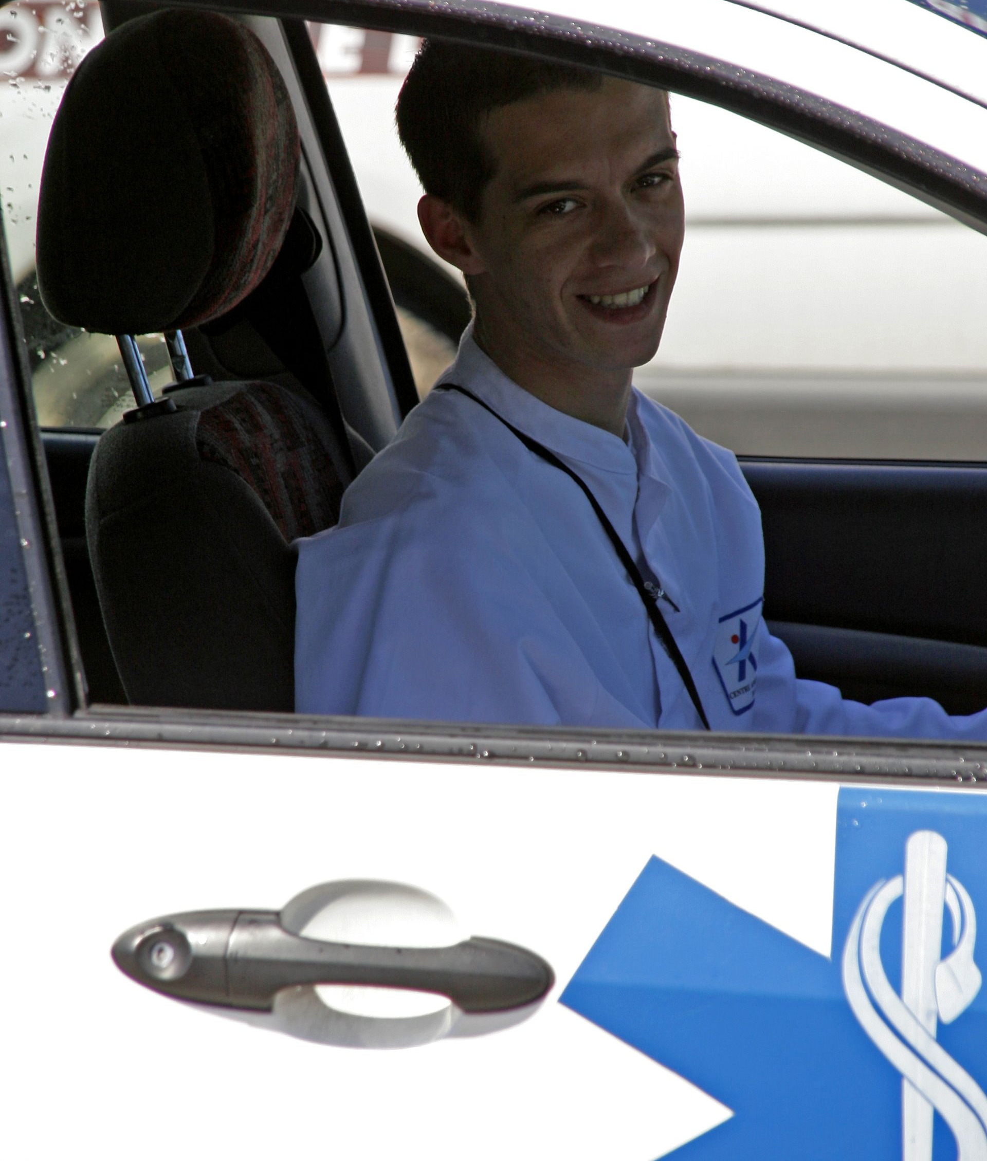 Un jeune homme assis dans une voiture portant une blouse