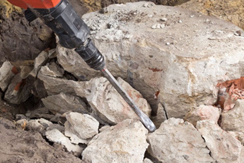 Eine Person benutzt einen Hammer, um einen Steinhaufen aufzubrechen.