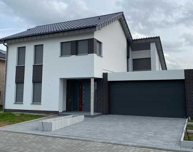 Ein weißes Haus mit einem schwarzen Garagentor und einer Backsteinmauer.