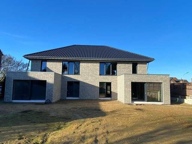 Ein großes Backsteinhaus mit schwarzem Dach steht auf einem üppigen grünen Feld.