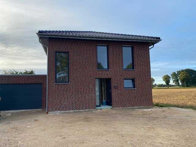 Ein Backsteinhaus mit einer Garage und vielen Fenstern steht auf einem Feld.