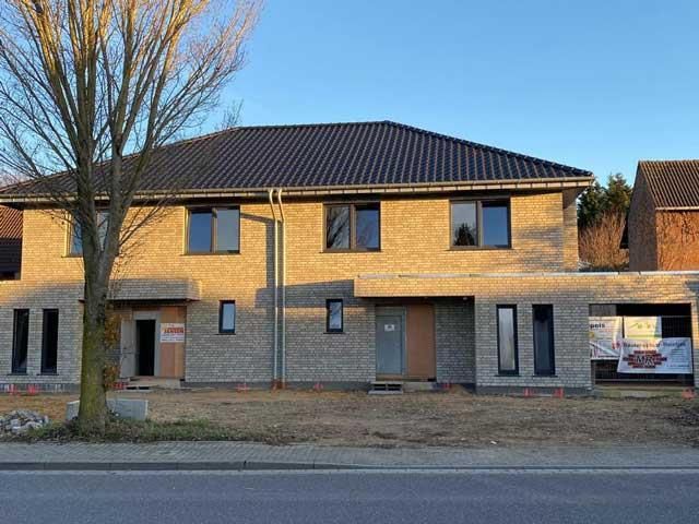 Ein Backsteinhaus mit schwarzem Dach und einem Baum davor.