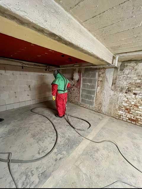 Ein Mann im Schutzanzug steht mit einem Staubsauger in einem Raum.