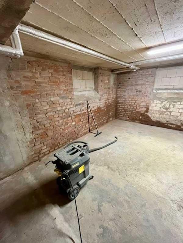 Ein Staubsauger steht in einem Keller neben einer Backsteinmauer.