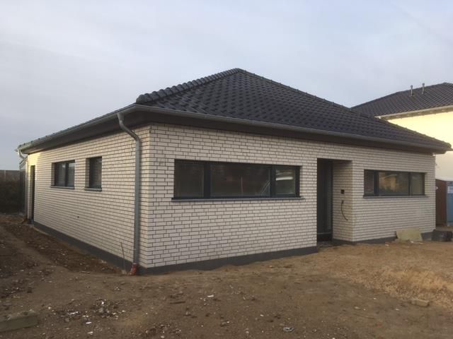 Ein kleines weißes Backsteinhaus mit schwarzem Dach und schwarzen Fenstern.