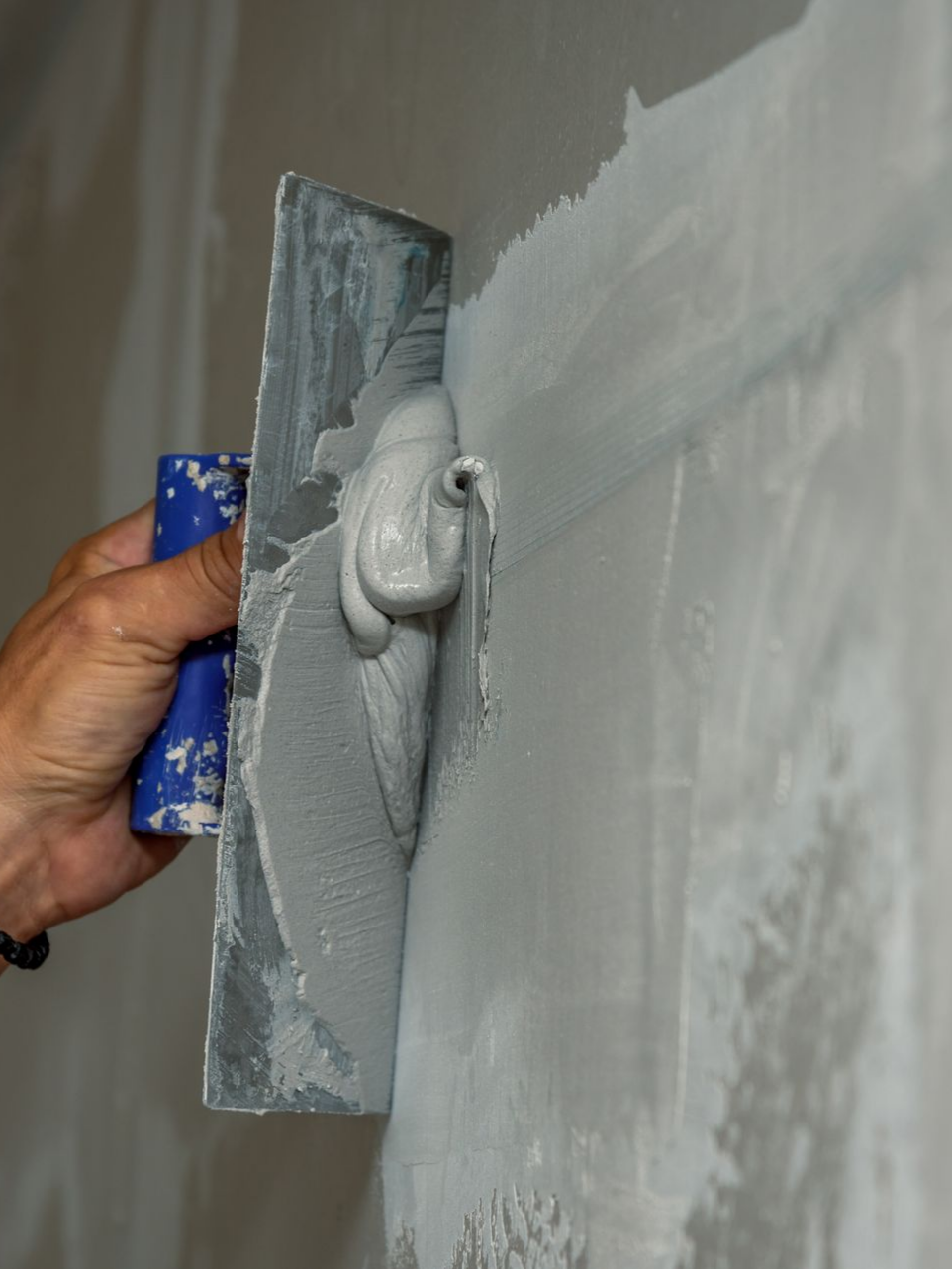 Personne utilisant un platoir pour appliquer un enduit à joints gris sur un mur.