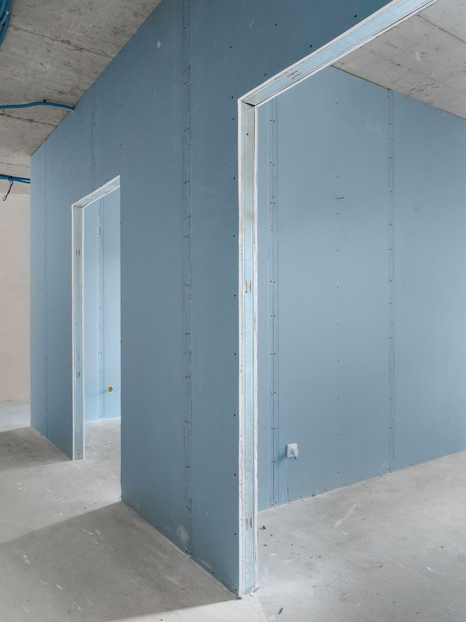 Aménagement intérieur avec murs en plaques de plâtre bleues et cadres de portes en métal.