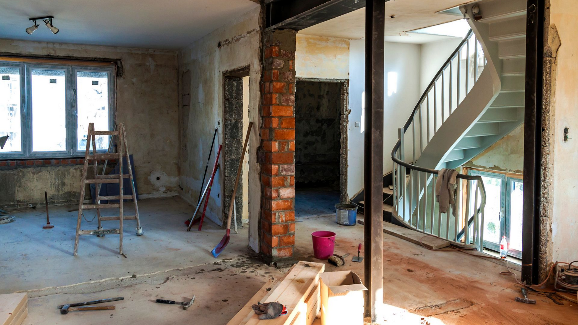 Pièce en rénovation ; pilier en briques apparentes, escalier et poutres de soutien visible.