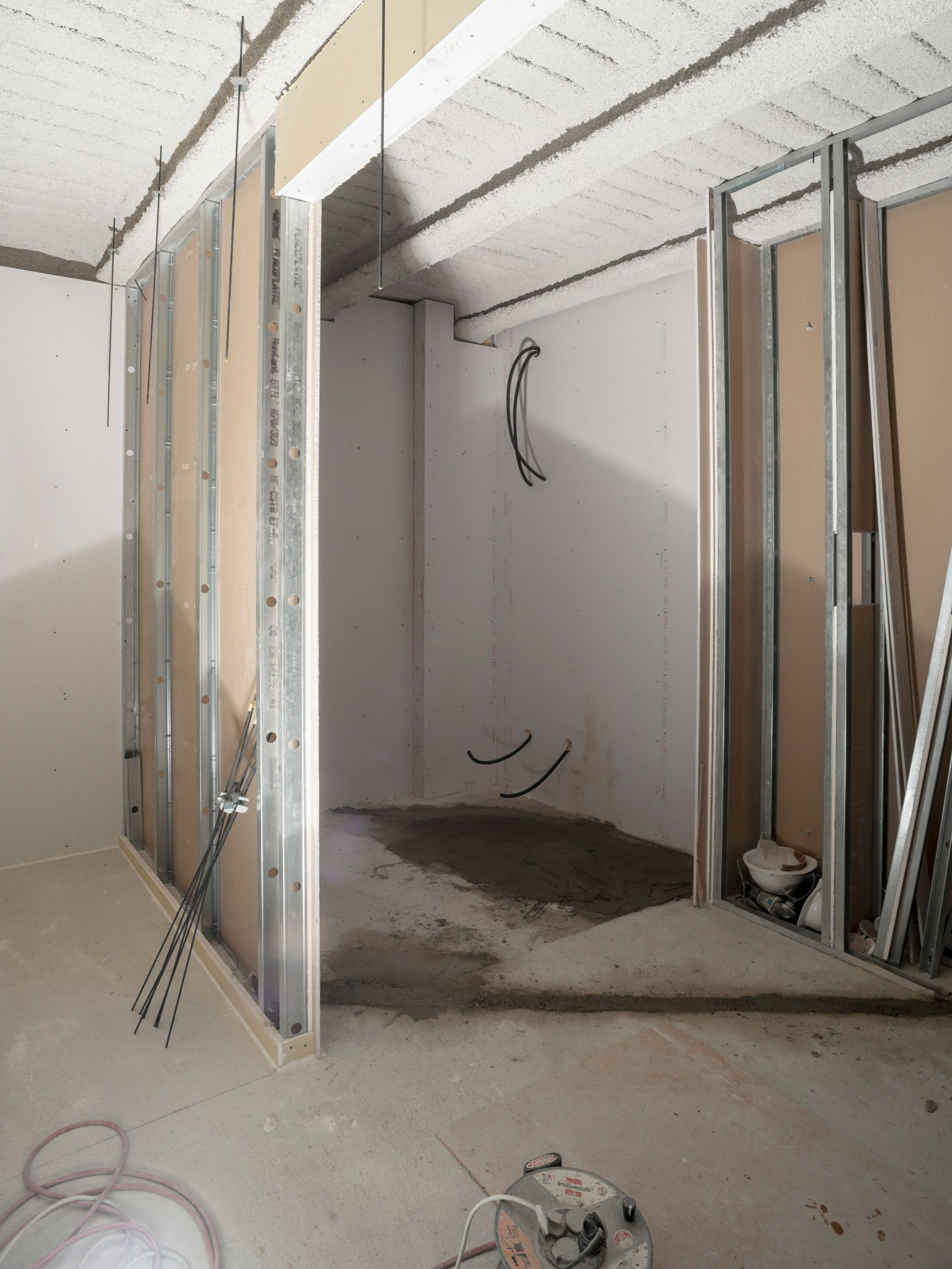 Intérieur en travaux : ossature métallique, murs et porte non finis, sol en béton.