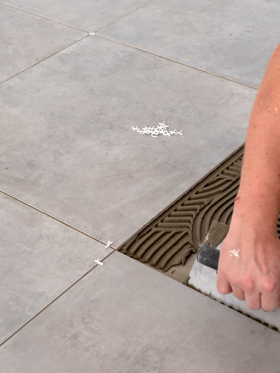 Personne utilisant une truelle pour appliquer du joint entre des carreaux gris.
