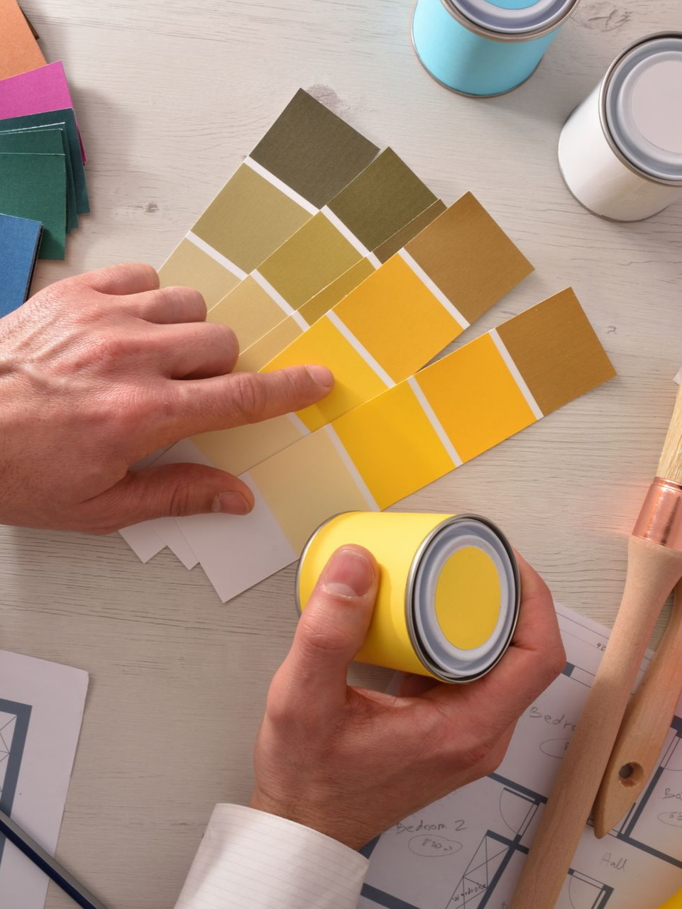 Une personne montre des échantillons de peinture. Des pots de peinture et des pinceaux sont disposés sur une table.