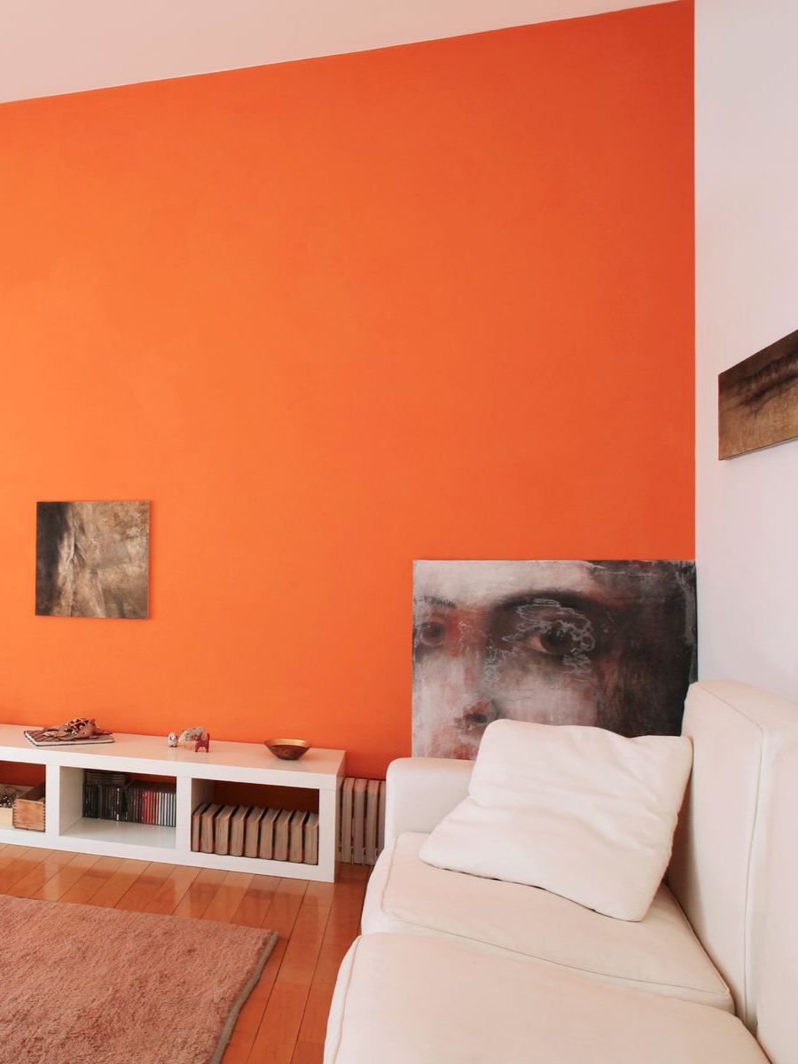 Salon avec mur orange, canapé blanc, œuvres d'art et meuble de rangement blanc.