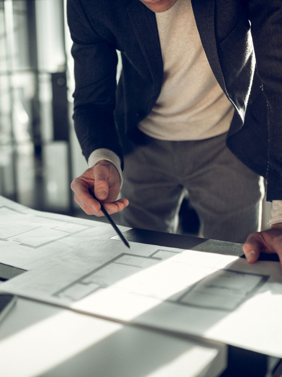 Une personne en blazer désigne du doigt des plans architecturaux posés sur une table.
