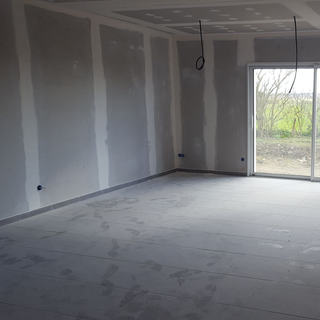 Intérieur d'une pièce en construction, avec des murs en plaques de plâtre et un sol en béton.