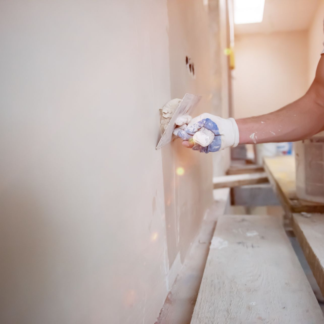 Une personne lissant un enduit mural à la truelle, portant des gants.