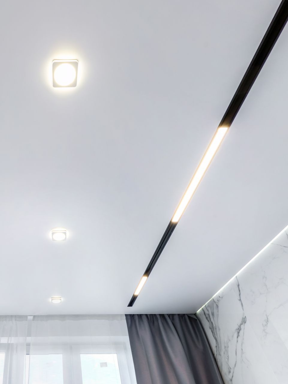 Plafond blanc avec trois spots encastrés et un long luminaire linéaire noir.