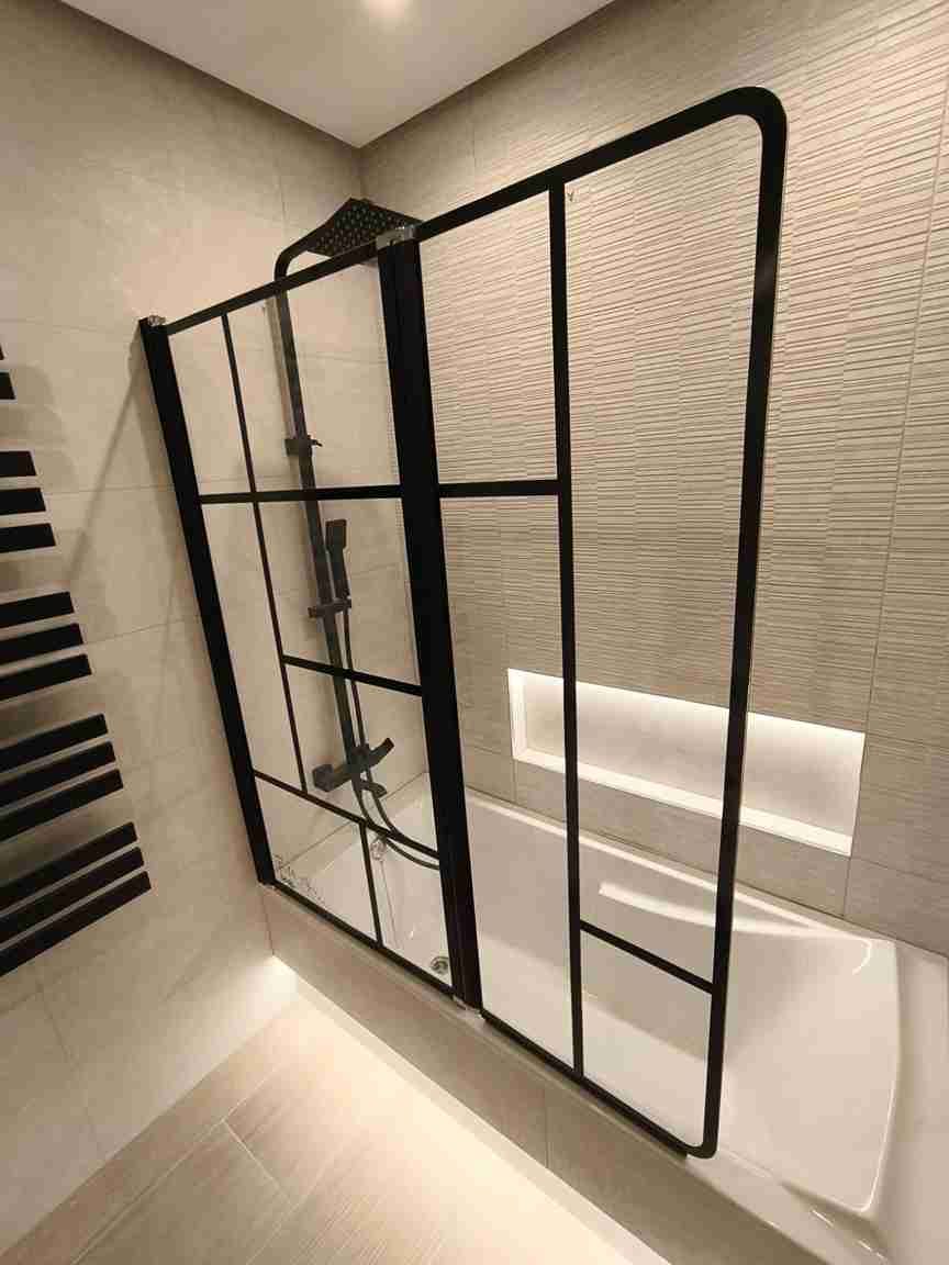 Mampara de ducha con marco negro sobre bañera. El baño tiene azulejos claros y toallero calefactado.