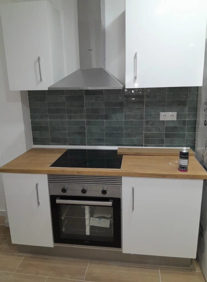 Cocina moderna con gabinetes blancos, encimera de madera, horno y protector contra salpicaduras verde.