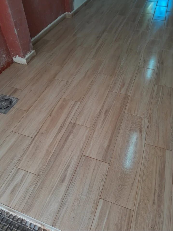 Suelo de baldosas imitación madera beige, colocadas de forma escalonada, en un pasillo con paredes rojas y blancas.