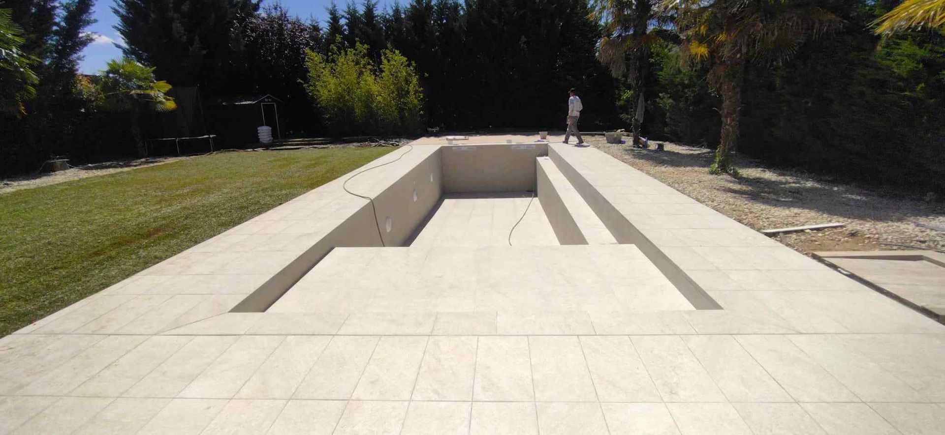 Piscina rectangular vacía en construcción, con patio de baldosas y jardín con césped.