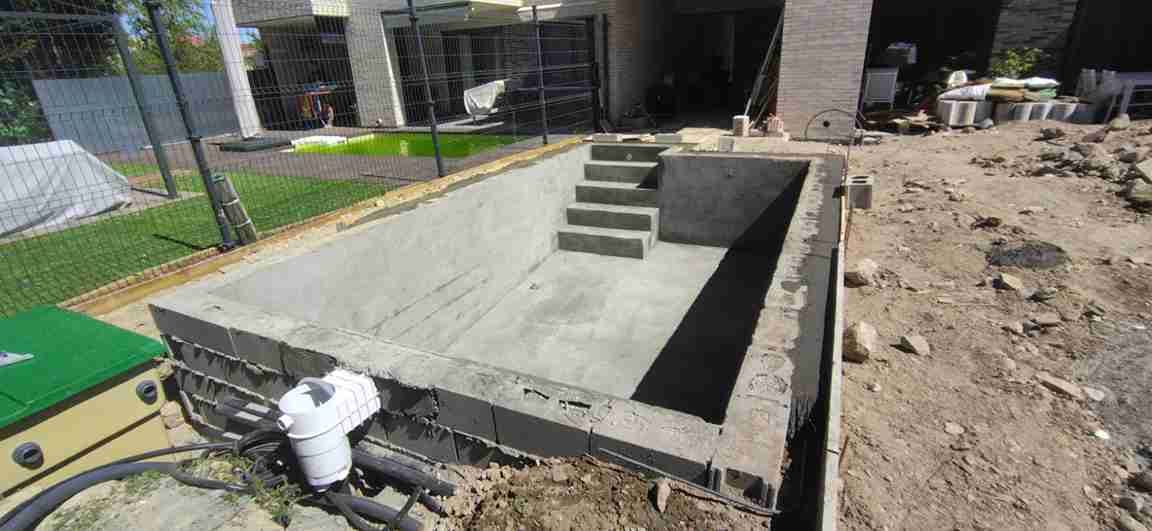 Una piscina de hormigón en construcción con escalones, rodeada de tierra y equipamiento.