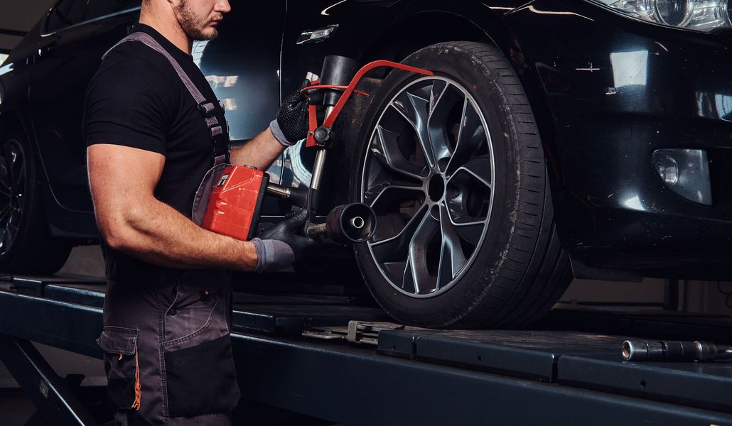 Um mecânico com uniforme escuro utiliza uma ferramenta de balanceamento de pneus em uma roda preta de um carro 