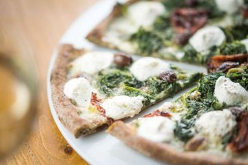 Eine Pizza mit Spinat und Mozzarella auf einem weissen Teller auf einem Holztisch.