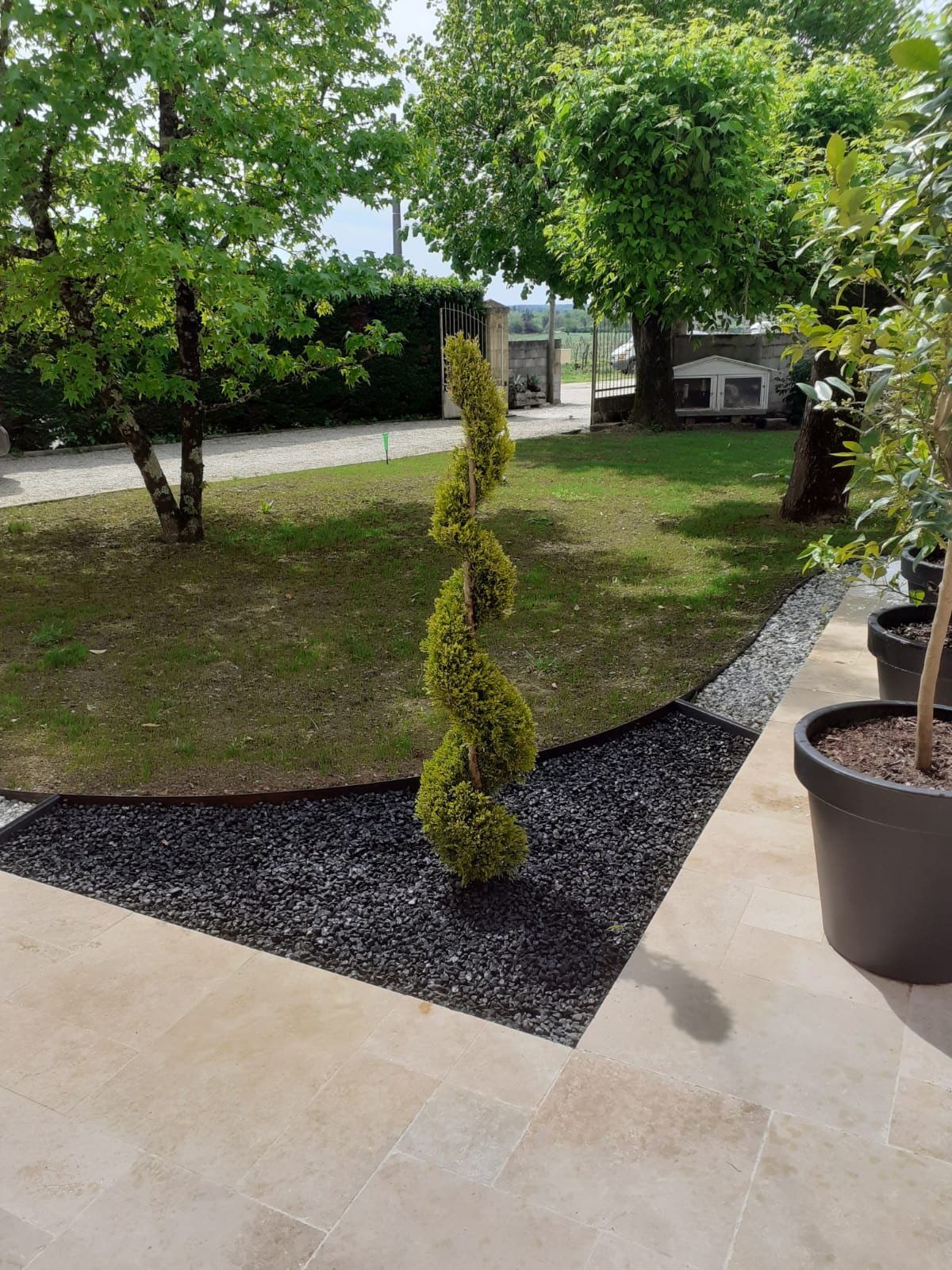 Un jardin avec une pelouse verte, des parterres de fleurs variées et colorées et des arbres denses.