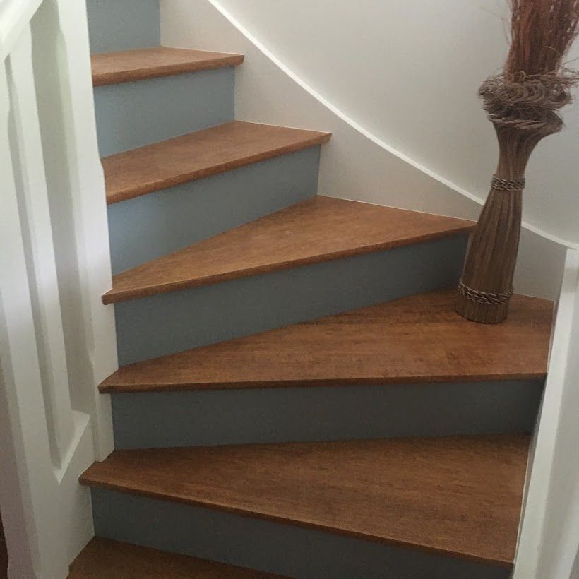 Escalier en bois courbé avec contremarches grises et un balai appuyé contre la rampe.