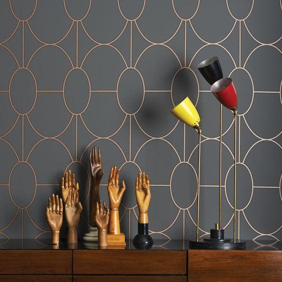 Sculptures de mains décoratives et lampes de table colorées sur un meuble en bois devant un papier peint gris à motifs