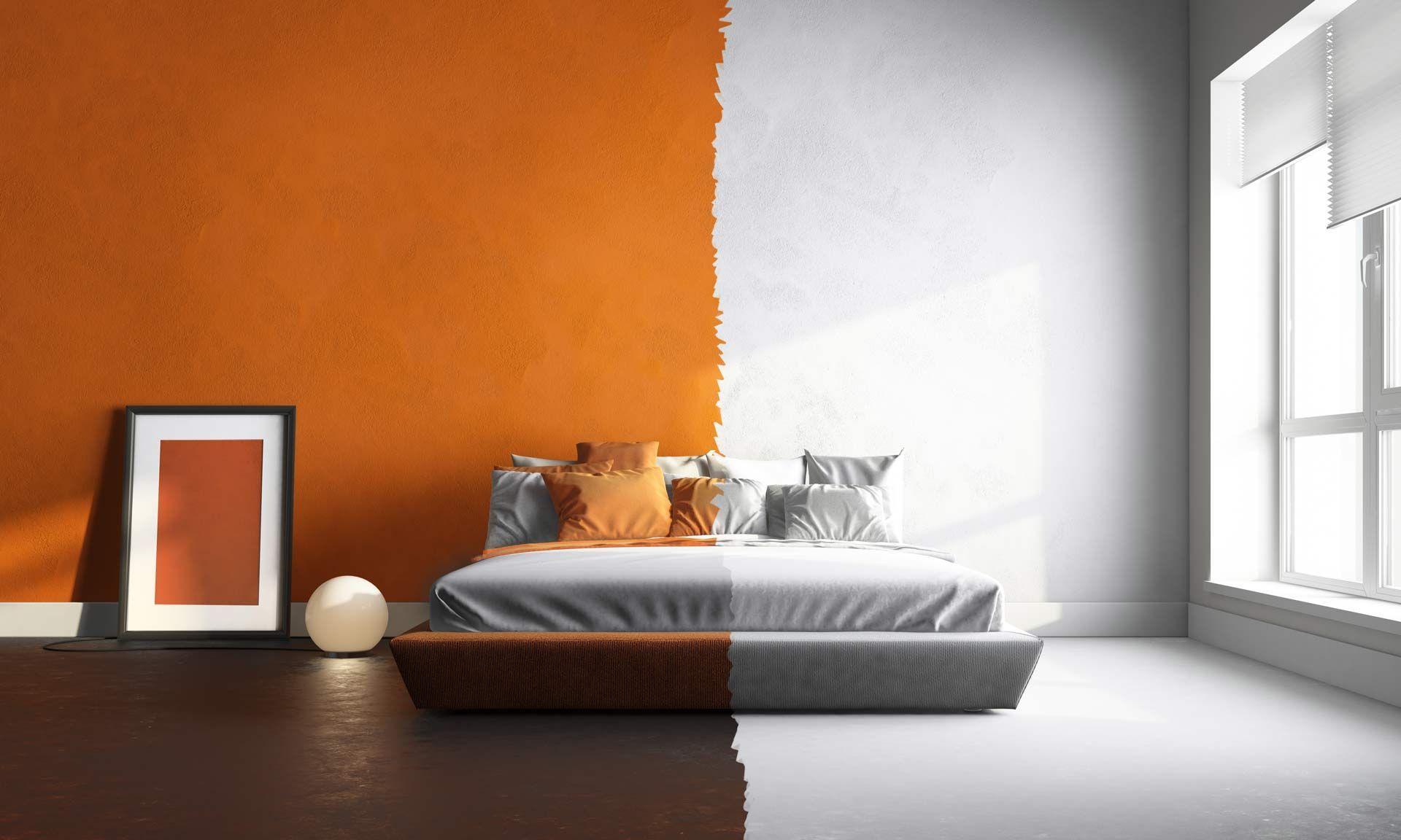 Chambre moderne aux murs orange et blancs, lit bas avec linge de lit gris et tableau encadré posé à même le sol