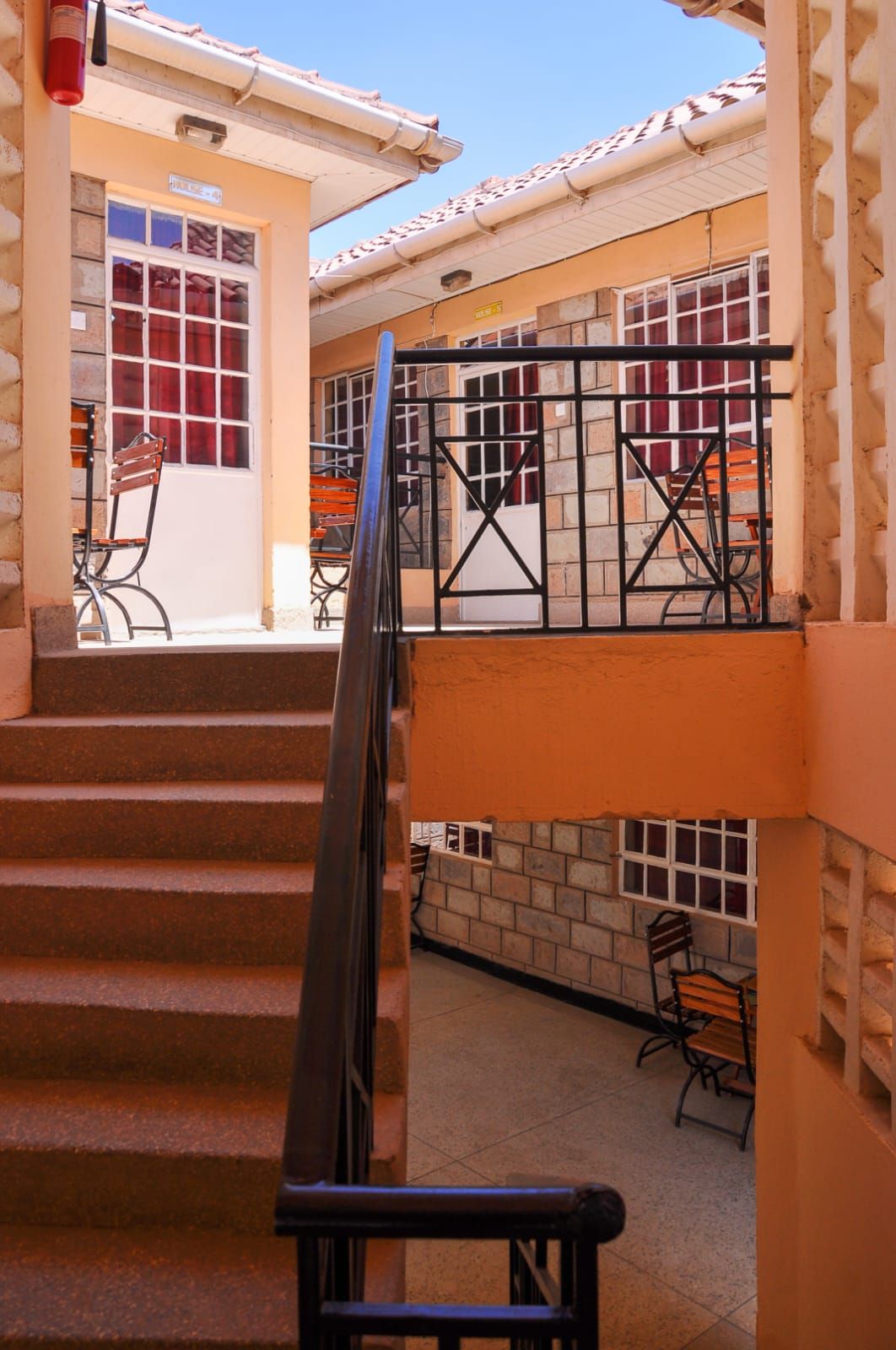 Stairway between tan stucco buildings with black railings and a red door, viewed from a courtyard.