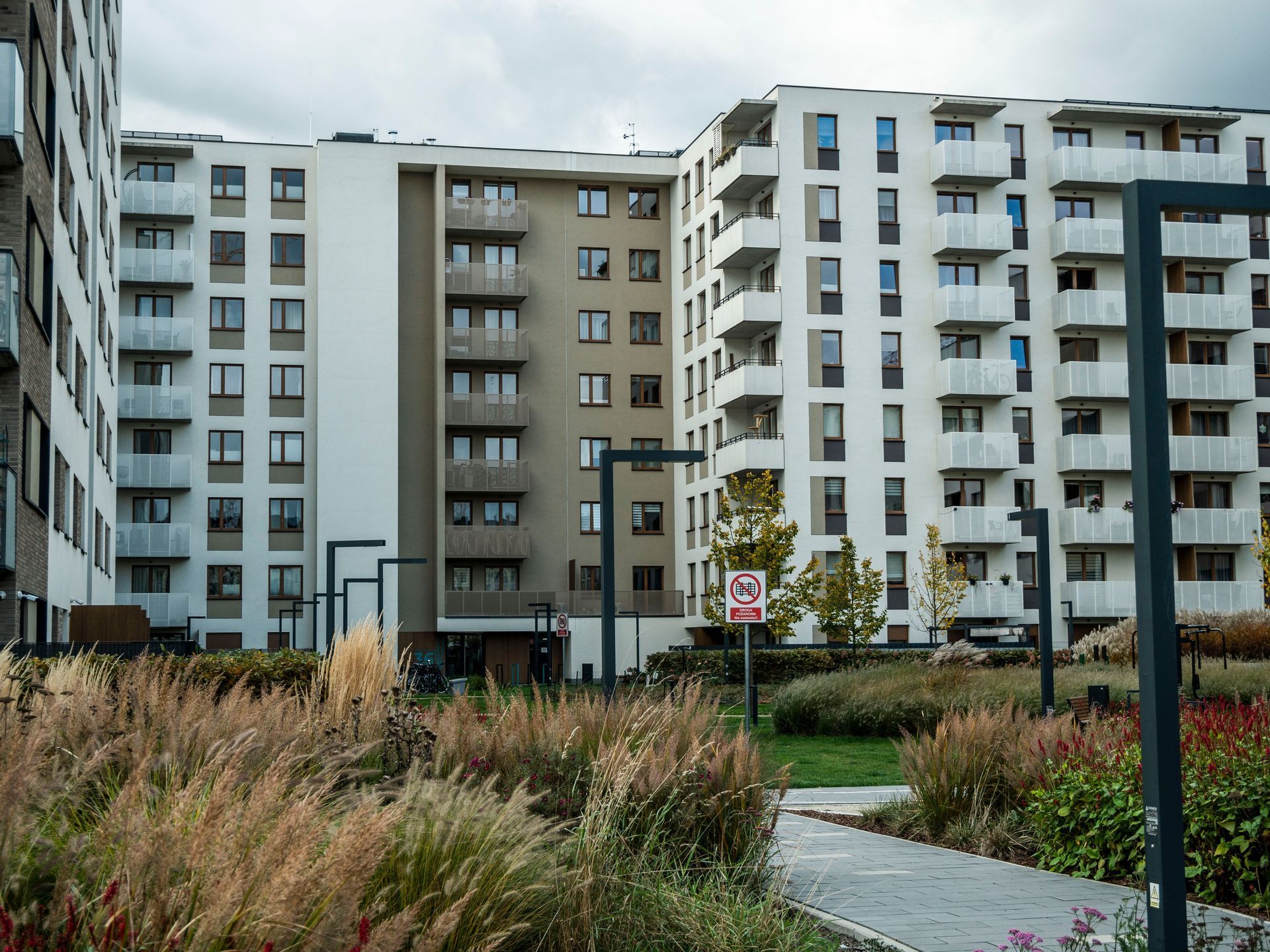 Modern apartment buildings behind a landscaped courtyard with tall grass and paved paths