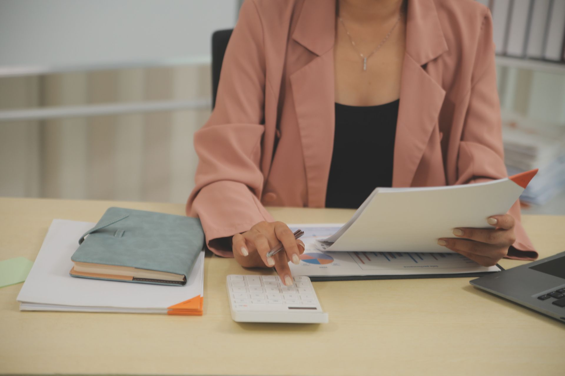 Una mujer con un blazer rosa hace cálculos con una calculadora en su escritorio.